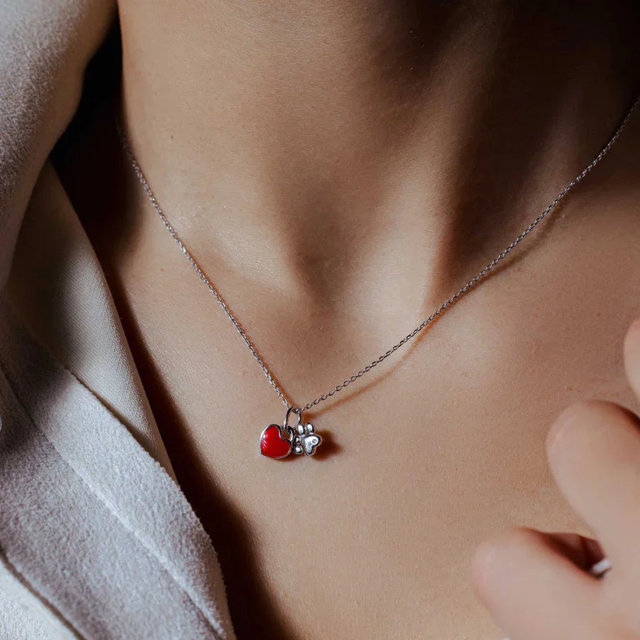 A close-up of the red enamel paw and heart necklace being worn.